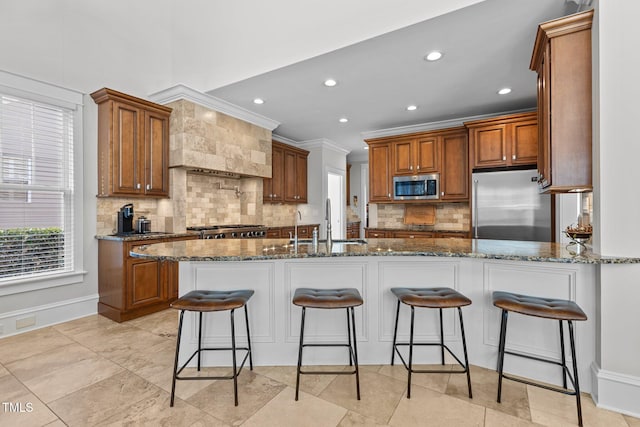 kitchen with stainless steel appliances, stone countertops, brown cabinets, and a kitchen bar