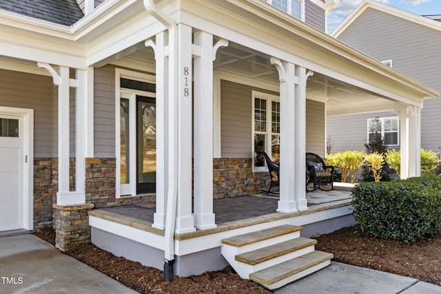 entrance to property with stone siding, covered porch, and roof with shingles