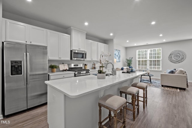 kitchen featuring a center island with sink, appliances with stainless steel finishes, dark wood-style flooring, white cabinetry, and a sink