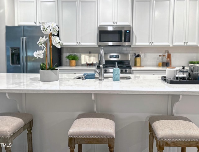 kitchen with white cabinets, light stone countertops, stainless steel appliances, a kitchen bar, and backsplash