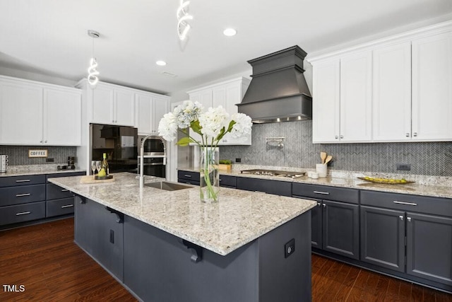 kitchen with dark wood-style flooring, a center island with sink, custom range hood, stainless steel gas stovetop, and white cabinets