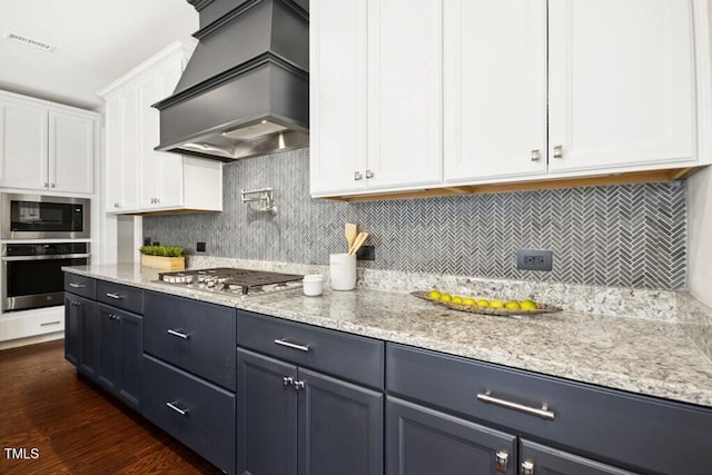 kitchen with visible vents, white cabinets, light stone counters, stainless steel appliances, and premium range hood