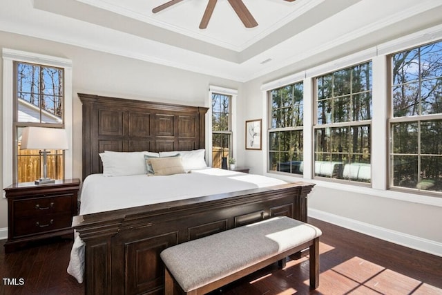 bedroom with ornamental molding, dark wood-type flooring, a raised ceiling, and baseboards