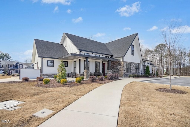 view of front of house featuring covered porch, stone siding, board and batten siding, and roof with shingles