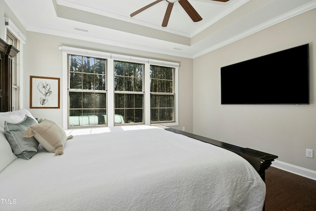 bedroom with a tray ceiling, wood finished floors, and ornamental molding