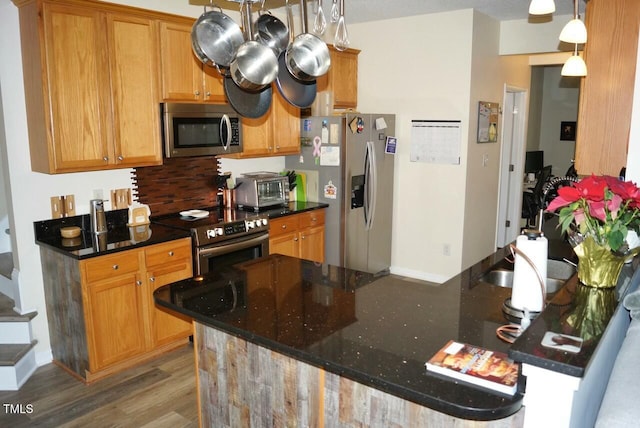 kitchen featuring stainless steel appliances, dark stone counters, baseboards, dark wood-style floors, and pendant lighting