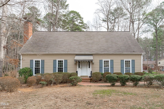 cape cod house with a shingled roof and a chimney