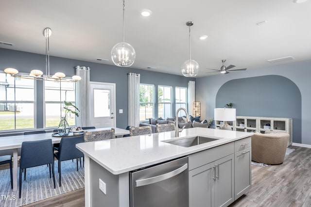 kitchen featuring sink, dishwasher, light hardwood / wood-style floors, hanging light fixtures, and a kitchen island with sink