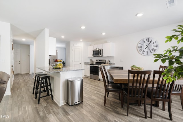 kitchen with visible vents, white cabinets, appliances with stainless steel finishes, light stone countertops, and light wood finished floors