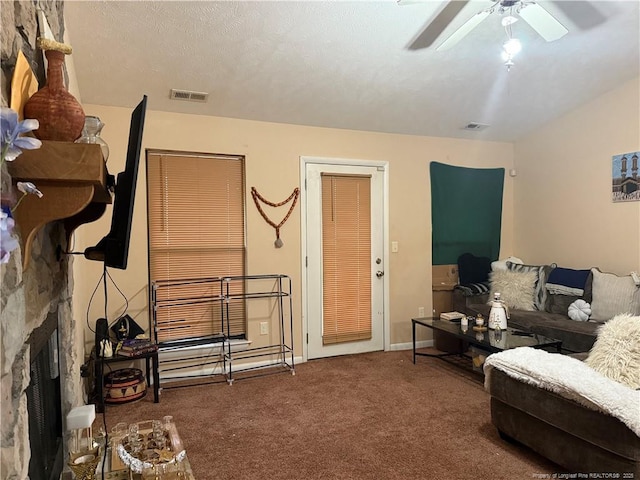 living room featuring carpet, ceiling fan, a stone fireplace, and a textured ceiling