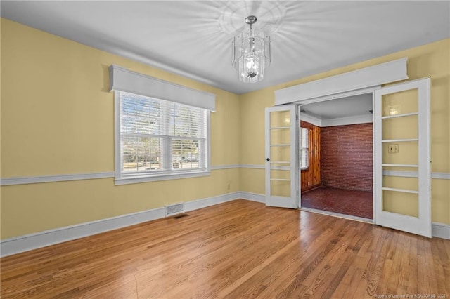 unfurnished room with a notable chandelier, french doors, and wood-type flooring