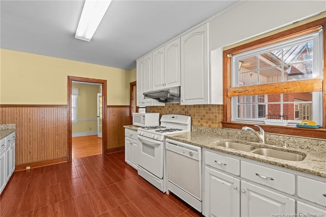 kitchen featuring white appliances, light stone counters, white cabinets, wood walls, and sink