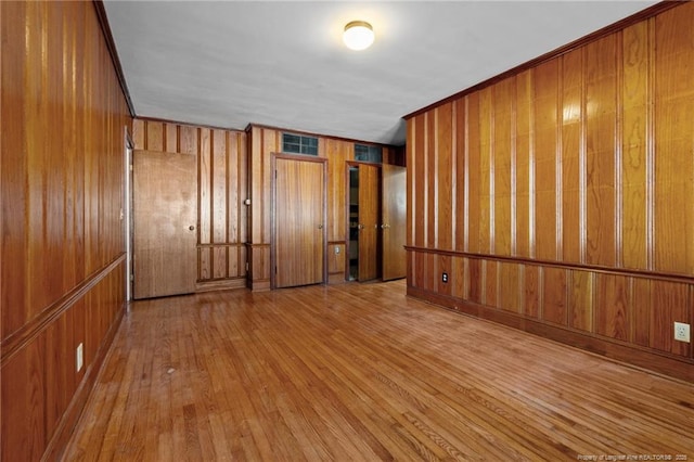 unfurnished room featuring light hardwood / wood-style flooring, wooden walls, and ornamental molding