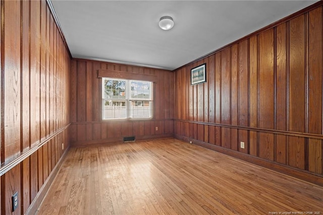 unfurnished room featuring light wood-type flooring and wood walls