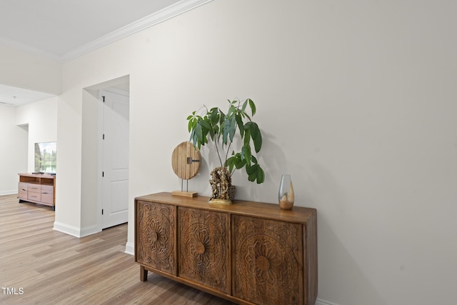 corridor with ornamental molding, light wood finished floors, and baseboards