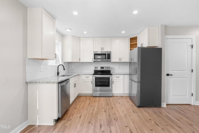 kitchen featuring light stone counters, light wood finished floors, a sink, stainless steel appliances, and white cabinets