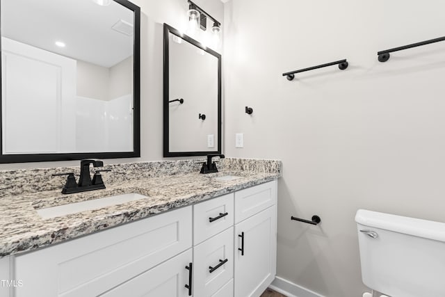 bathroom with double vanity, toilet, baseboards, and a sink