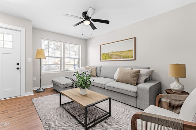 living room featuring baseboards, a ceiling fan, and light wood finished floors