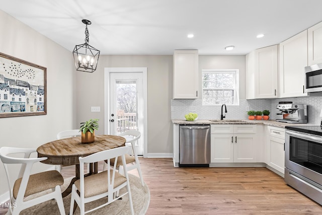 kitchen with light wood-style flooring, a sink, decorative backsplash, stainless steel appliances, and white cabinetry