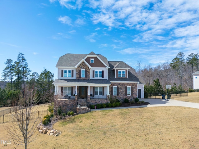 craftsman house with covered porch, driveway, a front yard, and fence