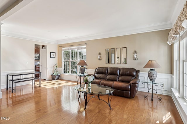 living area featuring a wainscoted wall, a decorative wall, light wood-type flooring, and crown molding