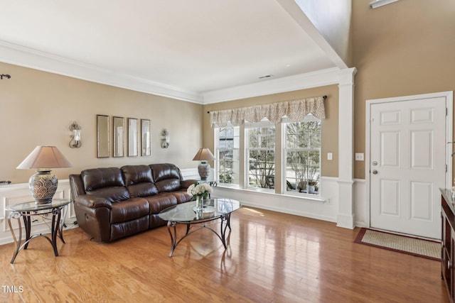 living room featuring decorative columns, visible vents, a wainscoted wall, ornamental molding, and light wood-type flooring