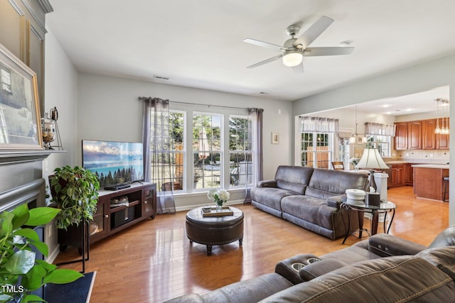 living room with ceiling fan, light wood-type flooring, visible vents, and baseboards