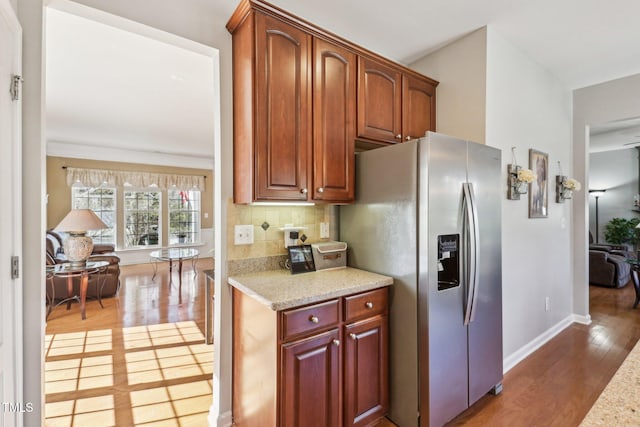 kitchen with light stone counters, decorative backsplash, wood finished floors, stainless steel fridge, and baseboards