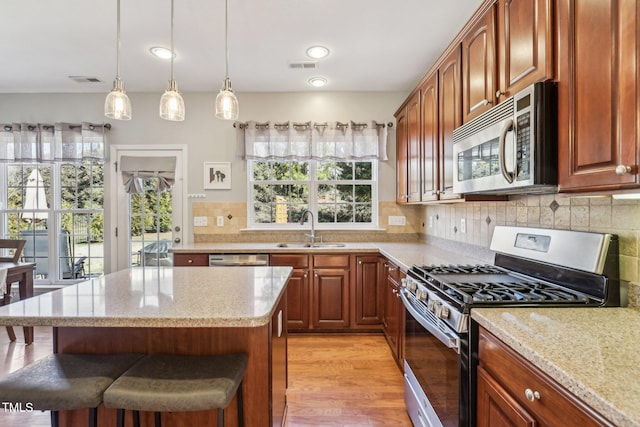 kitchen featuring tasteful backsplash, appliances with stainless steel finishes, decorative light fixtures, light stone countertops, and a sink