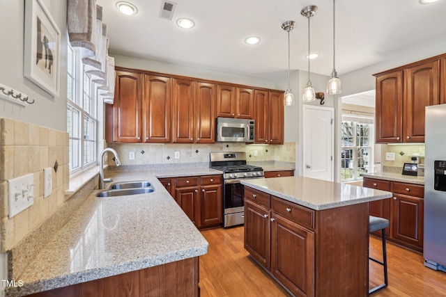 kitchen featuring a center island, stainless steel appliances, visible vents, hanging light fixtures, and a sink