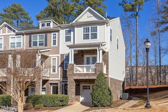 townhome / multi-family property with a garage, central AC unit, concrete driveway, a balcony, and stone siding