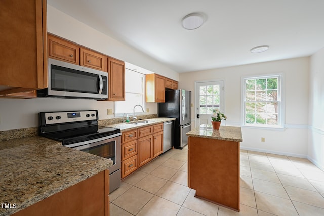 kitchen featuring brown cabinets, appliances with stainless steel finishes, a sink, and light stone countertops