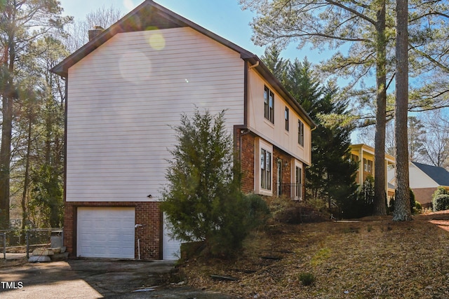 view of side of home featuring an attached garage, driveway, a chimney, and brick siding