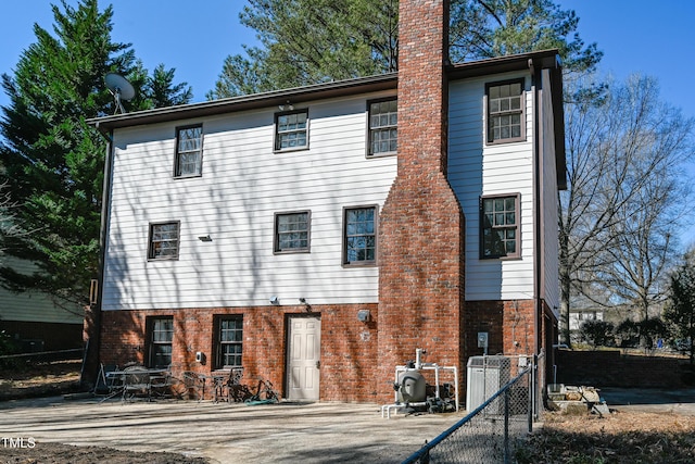 back of property with brick siding, a chimney, and fence