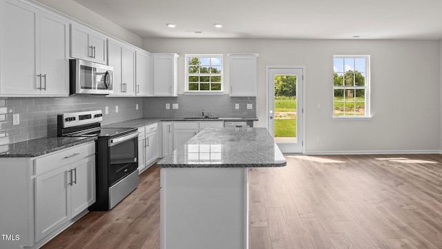 kitchen with white cabinets, a kitchen island, dark stone countertops, stainless steel appliances, and a sink