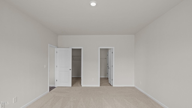 unfurnished bedroom with light carpet, a spacious closet, and baseboards