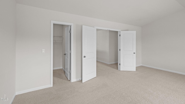 unfurnished bedroom with light carpet, a closet, a walk in closet, and baseboards