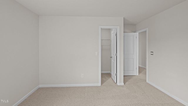 unfurnished bedroom with baseboards, a walk in closet, a closet, and light colored carpet