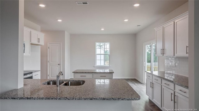 kitchen featuring white cabinetry, a center island with sink, sink, backsplash, and stone countertops