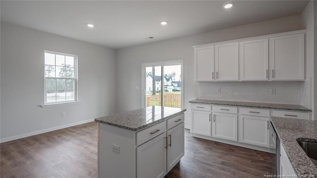 kitchen with white cabinetry, light stone countertops, a kitchen island, and dark hardwood / wood-style floors