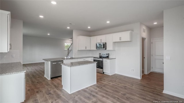 kitchen featuring wood-type flooring, stainless steel appliances, white cabinets, a center island, and kitchen peninsula