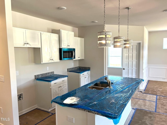 kitchen with stainless steel microwave, a sink, white cabinets, a center island with sink, and a wainscoted wall