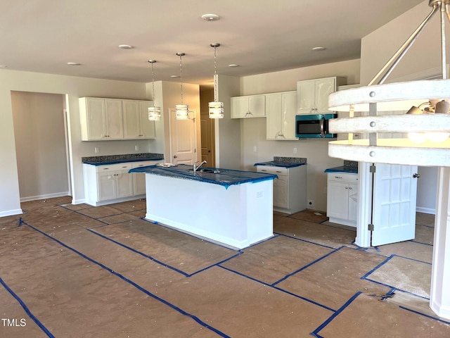 kitchen with white cabinetry, dark countertops, baseboards, and a kitchen island with sink