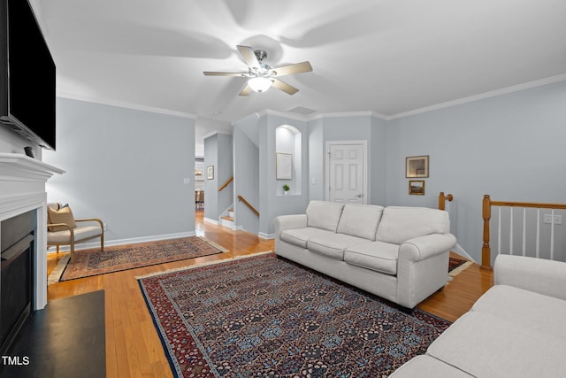 living room featuring a fireplace, ornamental molding, a ceiling fan, wood finished floors, and baseboards