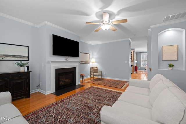 living area featuring ornamental molding, visible vents, light wood-style flooring, and a fireplace with flush hearth