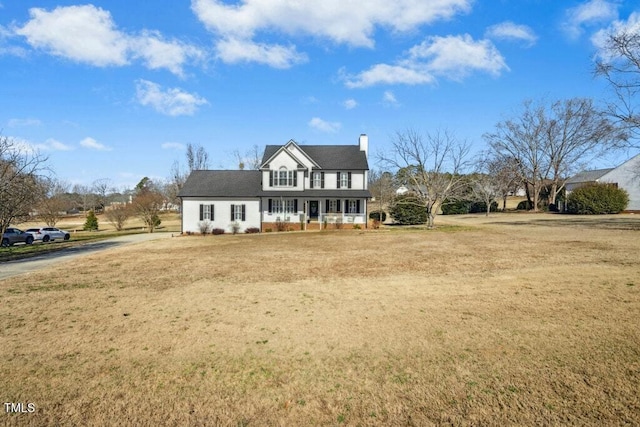 view of front of house with covered porch, a chimney, and a front yard