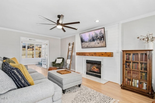 living area with ceiling fan, a warm lit fireplace, crown molding, and wood finished floors