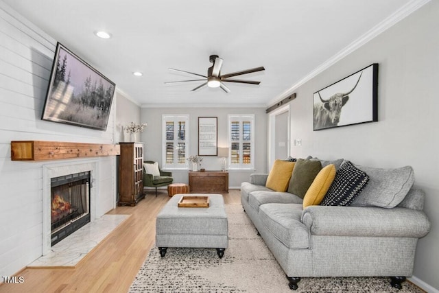 living area with a barn door, a premium fireplace, wood finished floors, a ceiling fan, and ornamental molding