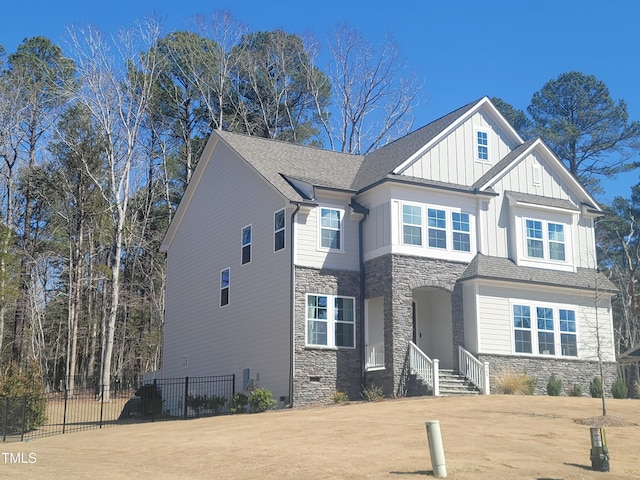 craftsman-style home with board and batten siding, a shingled roof, fence, a front yard, and stone siding