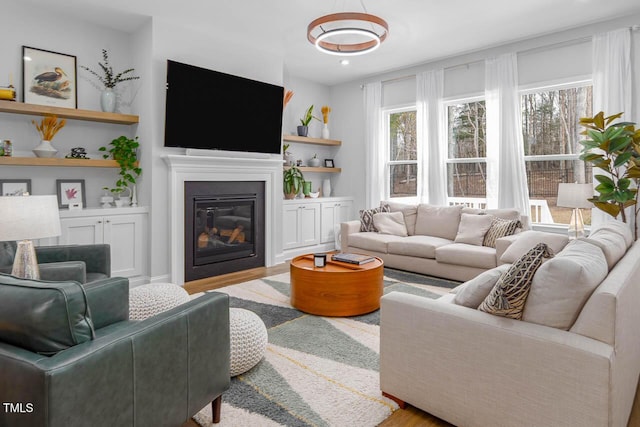 living room featuring a glass covered fireplace, built in features, and wood finished floors